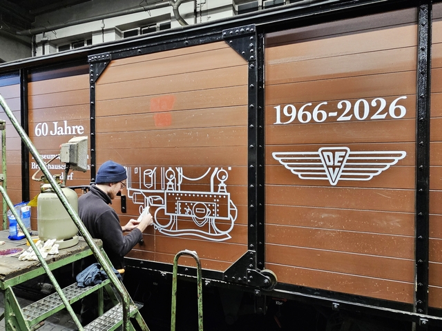 Abb.: Sieht doch schon gut aus! Langsam wird Lok HOYA auf dem Wagen sichtbar. DEV Werbetechnikermeister Peter Ptak, der die Klebefolien vorbereitete, war über die Ausführung der Beklebung begeistert: toller Job der Beiden und das bei den Temperaturen! (Klicken vergrößert).